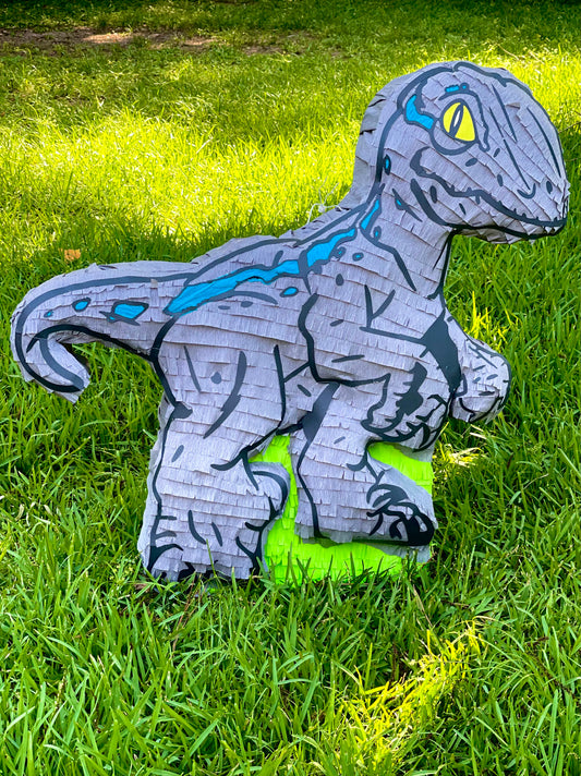 Handcrafted blue and grey raptor dinosaur piñata with 3D relief texture on grass background
